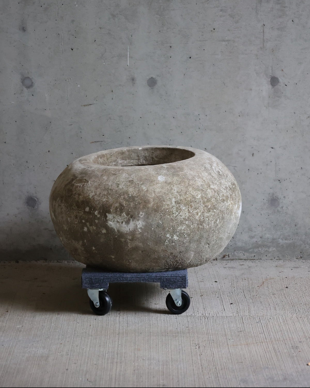 A large round stone planter or vase with a rough, weathered texture